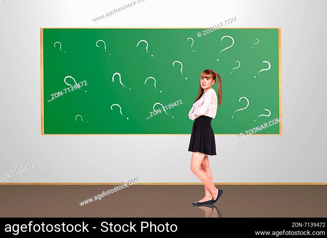Scoolgirl standing in the classroom near a green blackboard
