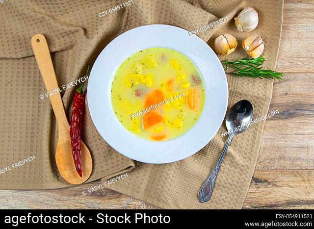Potato cream soup with mushrooms, carrots and cheese. Top view. The plate is on a coffee towel, there is a spoon next to it