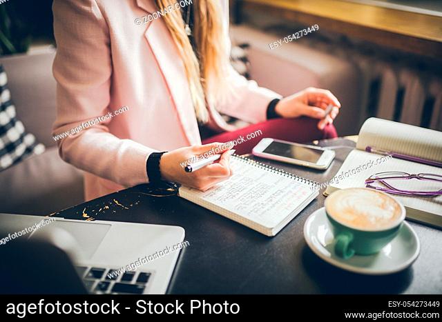 Close up caucasian woman hand on wooden table inside cafe makes notes in notebook. Subject freelancer blogger journalist at work