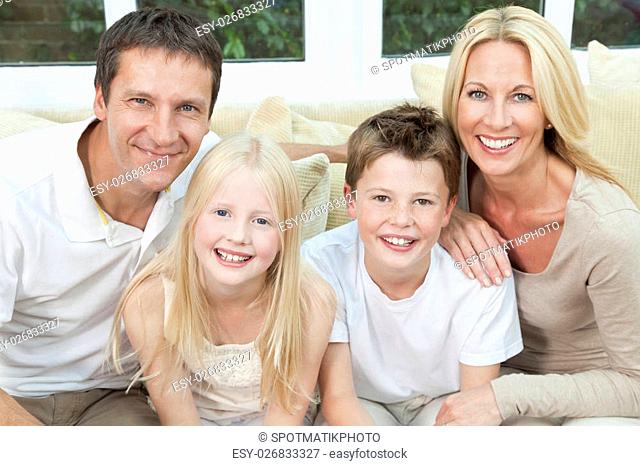 An attractive happy family of mother, father, son and daughter sitting on a sofa at home having fun