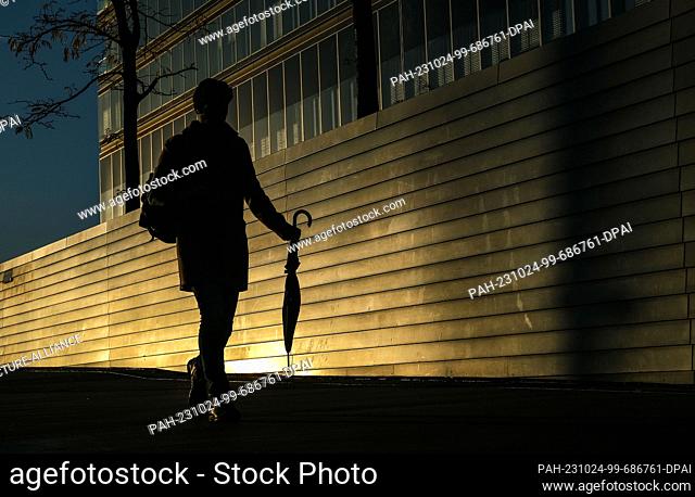 24 October 2023, North Rhine-Westphalia, Cologne: A man walks along an office building reflecting the evening sun after a rainy day