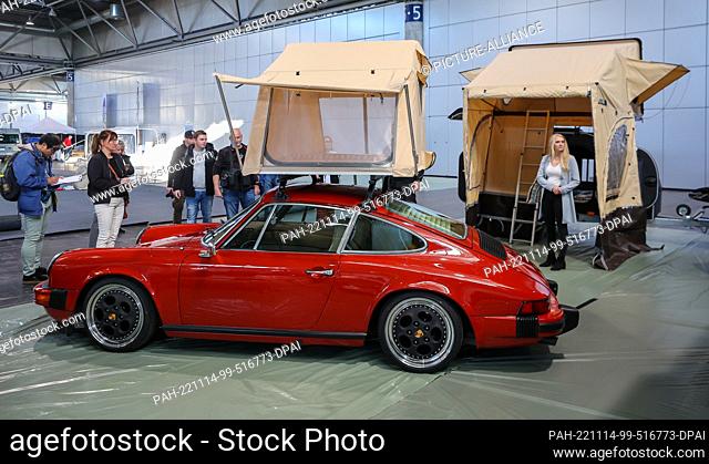 14 November 2022, Saxony, Leipzig: Journalists stand around a Porsche with a roof tent from the company Stray Camp in an exhibition hall during a press event