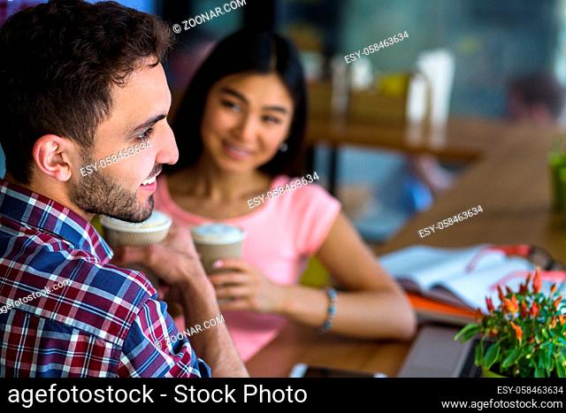 Closeup picture of handsome man looking away while listening to his girl-friend. Romantic couple in love having date. People drinking coffee and communicating