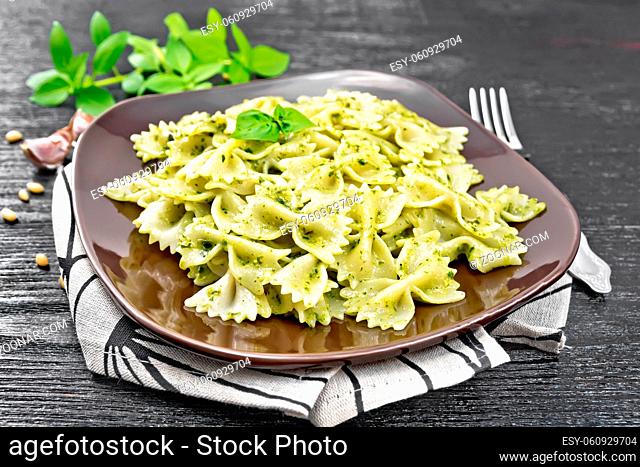 Farfalle pasta with pesto, basil in a plate on a towel on wooden board background