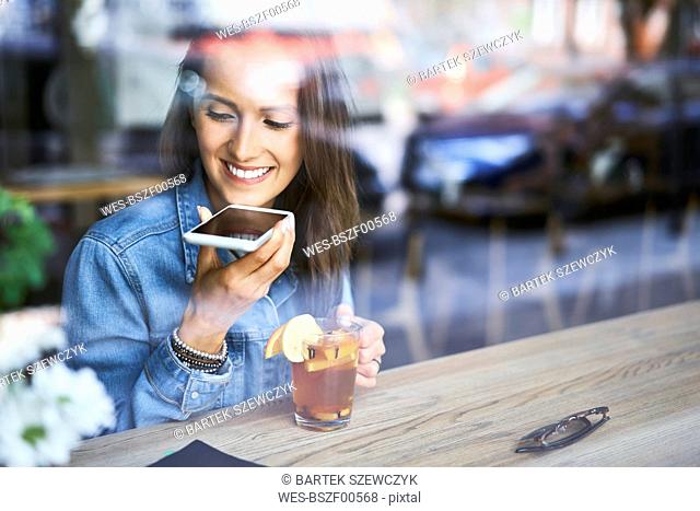 Smiling young woman speaking on phone in cafe while having tea