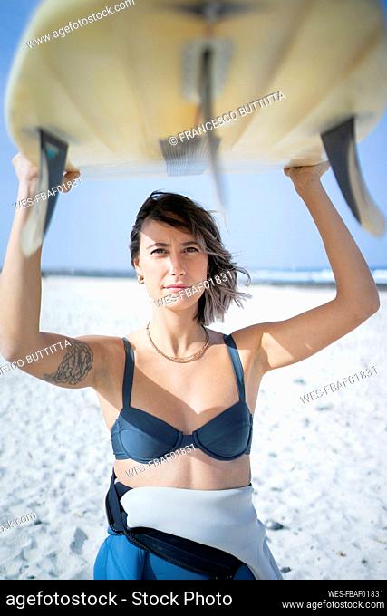 Young woman in bikini carrying surfboard at beach