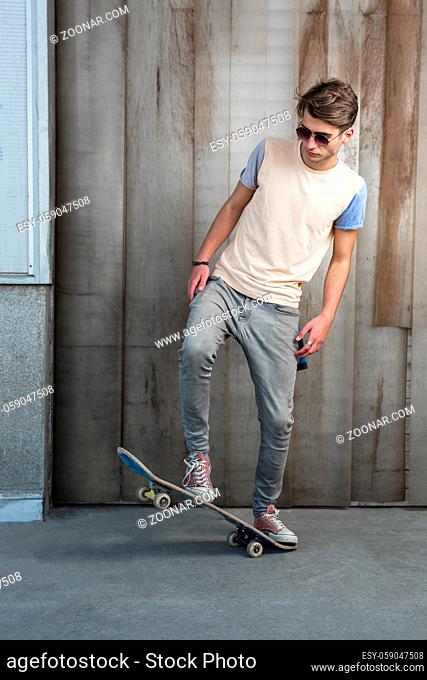 Handsome man posing with skateboard near the wall