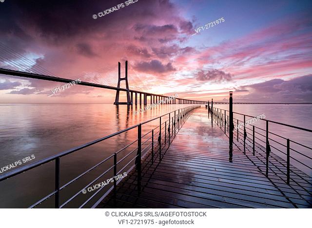 Sunrise colors the clouds reflected in Tagus River and frame the Vasco da Gama bridge in Lisbon Portugal Europe