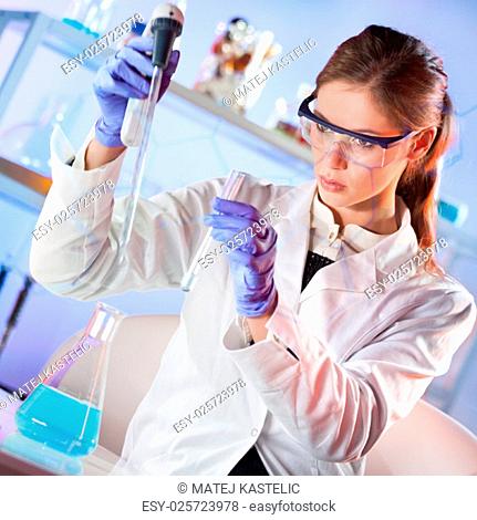 Life scientists researching in laboratory. Focused female life science professional pipetting blue solution into glass cuvette