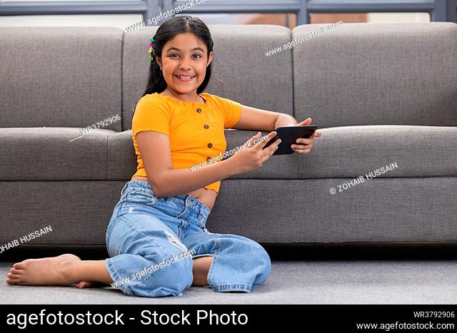 Portrait of a cheerful girl looking at camera while using digital tablet at home