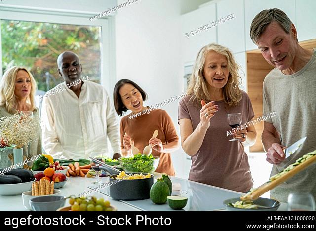 Diverse group of senior friends gathered at kitchen while cooking