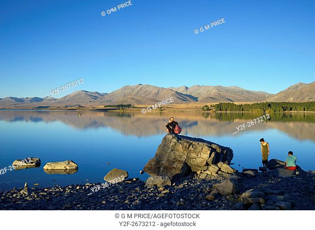 travellers sit by Lake Tekapo, New Zealand
