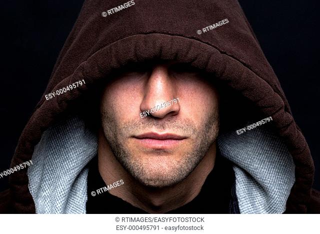 An evil looking man wearing a hooded top with his eyes hidden against a black background