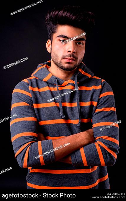 Studio shot of young handsome Indian man against black background