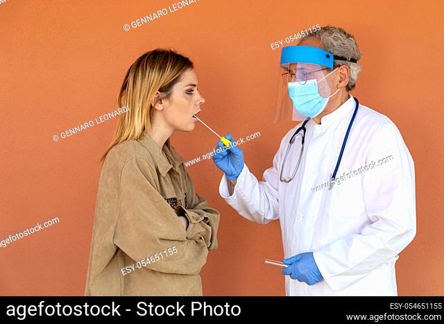 Doctor takes a sample from the throat of a young woman, for subsequent laboratory analysis in search of the SARS-CoV-2 virus