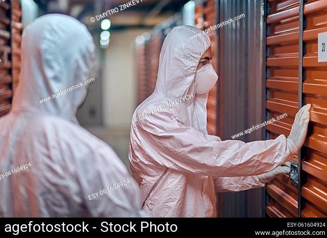 Concentrated warehouse worker in the protective equipment opening the container door in the presence of a customer