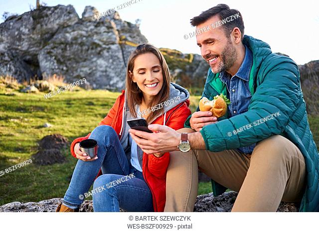 Happy couple on a hiking trip in the mountains taking a break looking at cell phone