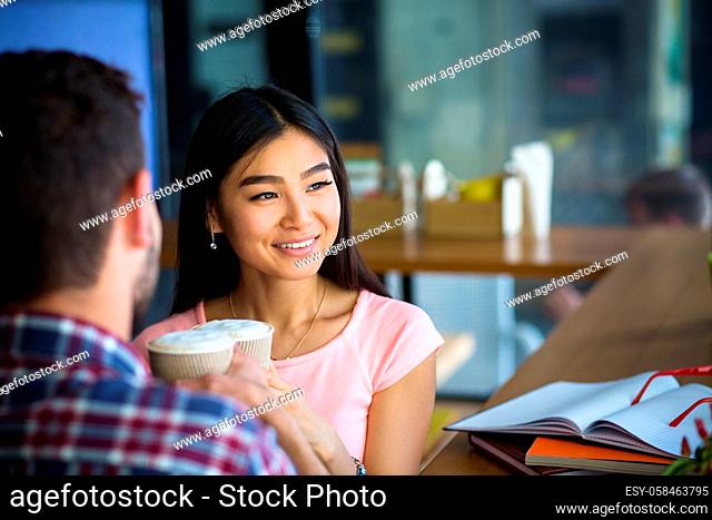 Romantic couple having date in restaurant or cafe. People drinking coffee. Asian or Korean lady looking into window