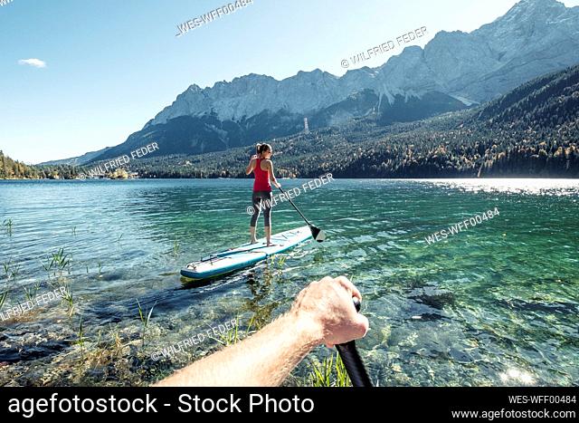 Germany, Bavaria, Garmisch Partenkirchen, Young couple stand up padling on Lake Eibsee, overlooking Zugspitze Mountain