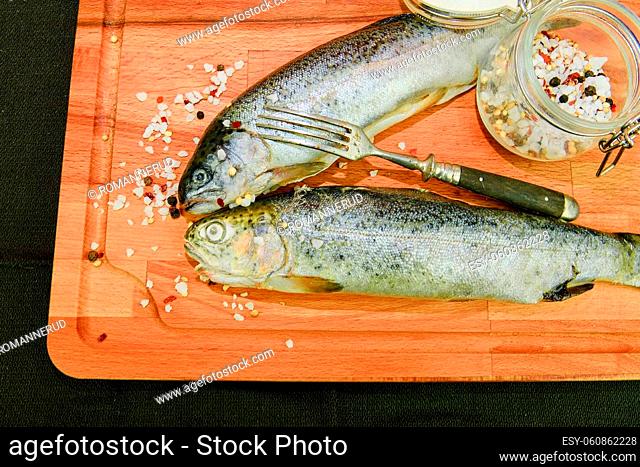Fresh raw rainbow trouts with spices and fork on wooden board. Healthy food and dieting concept. Close-up