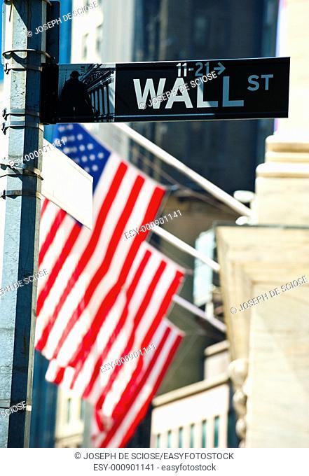 Wall Street sign with the New York Stock Exchange building and American flags in the background in the financial district in New York City