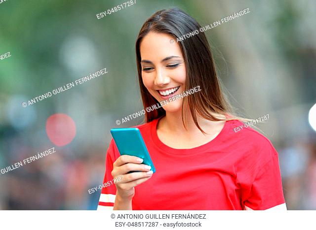 Happy woman in red reads a message on a smart phone in the street