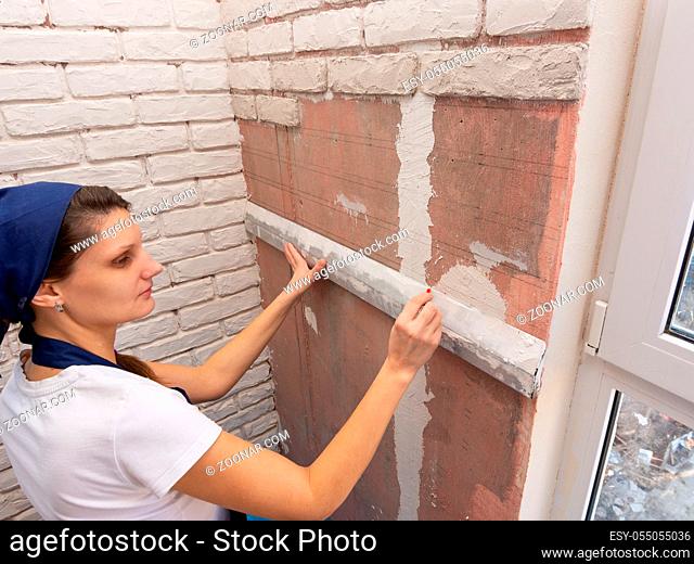 Plasterer applies a horizontal line with a pencil on the wall using aluminum rule