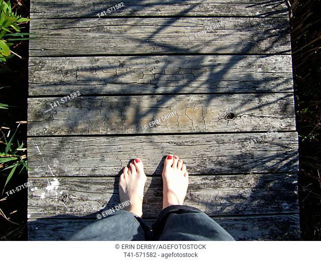 Bare feet on a dock in Mattituck, NY. Mattituck is on the South Shore of the North Fork of Long Island. The feet are of a woman, with half worn polish