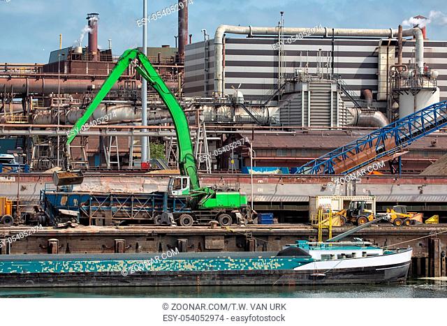 Big steel factory in harbor IJmuiden with crane unloading a barge, The Netherlands