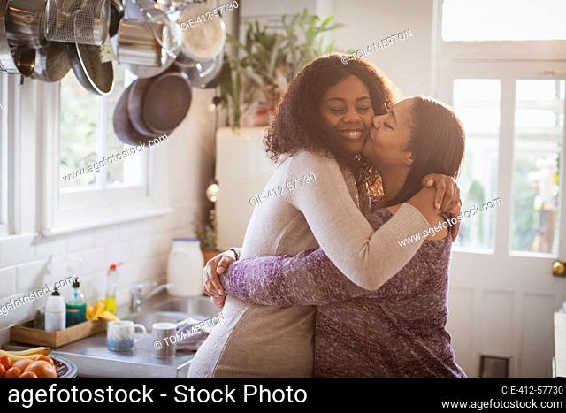 Madre e hija abrazándose y besándose en la cocina