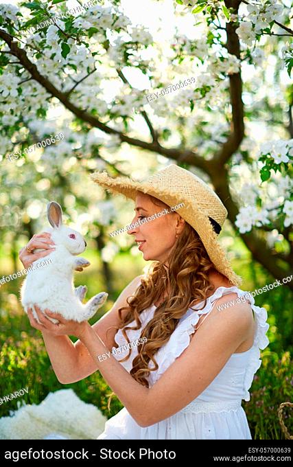 The beautiful girl with white rabbit in the blossoming apple-trees garden. White flowers in a garden in sunshine. Spring apple trees in blossom