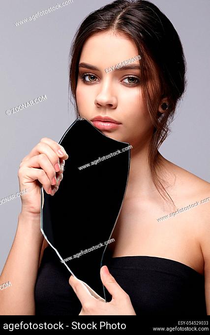 Girl with a shard of the mirror. Female with mirror shard in hand posing on gray background