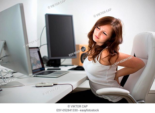 Woman working on a computer in a home office - suffering form lower back pain