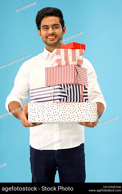 A YOUNG MAN HAPPILY STANDING WITH GIFTS IN HAND