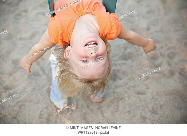 A child playing outdoors. A girl hanging upside down on a swing