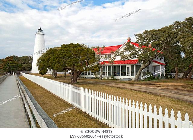 White picket fence and walkway lead past the red-roofed keepers quarters towards the tower of the Ocracoke Island lighthouse on the outer banks of North...