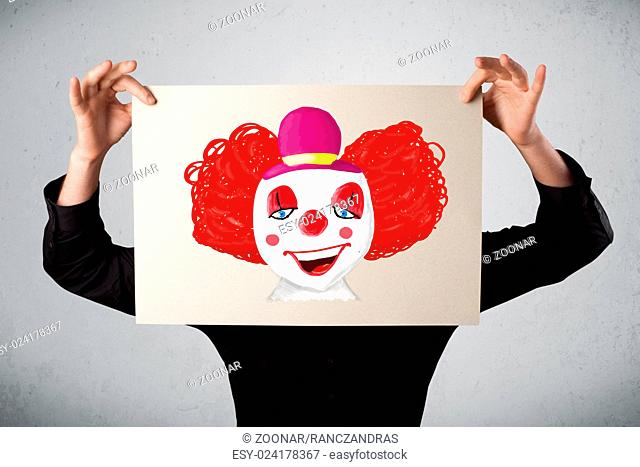 Businessman holding a cardboard with a clown on it in front of his head