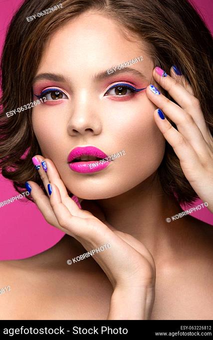 Beautiful model girl with bright makeup and colored nail polish. Beauty face. Short colorful nails. Picture taken in the studio on a pink background
