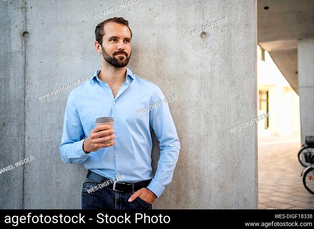 Young businessman with coffee cup standing in front of wall