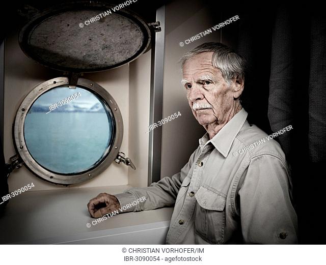 Elderly man stands in ship's cabin with a thoughtful expression