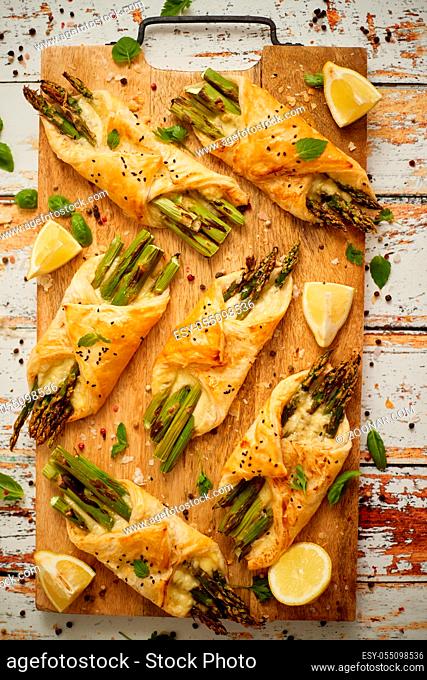 Grilled green asparagus and cheese puff pastry folded as envelope and topped with black sesame seeds placed on wooden cutting board