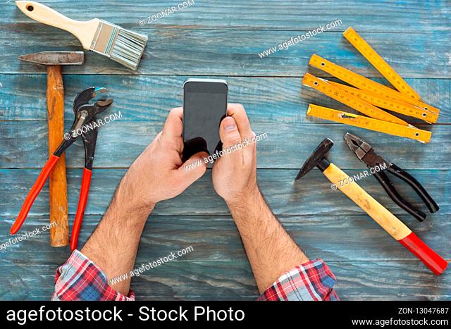 Man working on a DIY project with his phone, wood shavings and carpentry tools and construction all around, top view