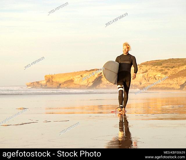 Male surfer with surfboard walking at beach against sky