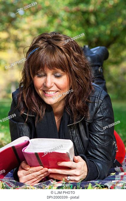 young woman reading the bible and meditating in a park, edmonton alberta canada