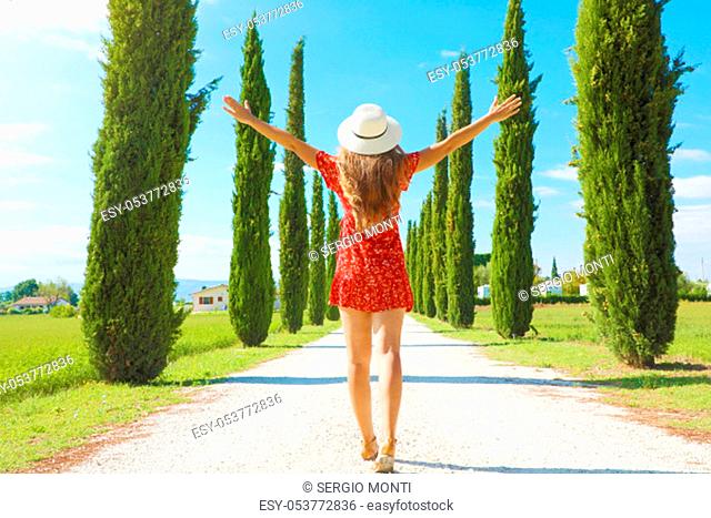 Flying in Tuscany concept. Young woman walking in beautiful and idyllic landscape of a lane of cypresses in the Italian countryside of Tuscany