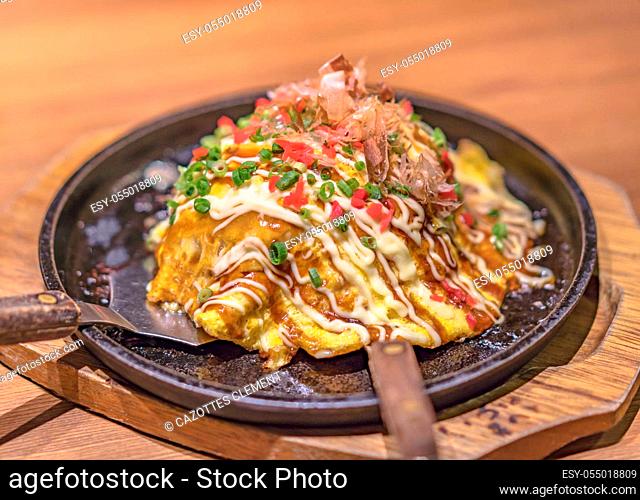 Japanese okonomiyaki covered with katsuobushi leek mayonnaise and bulldog sauce served on a hot plate with spatulas
