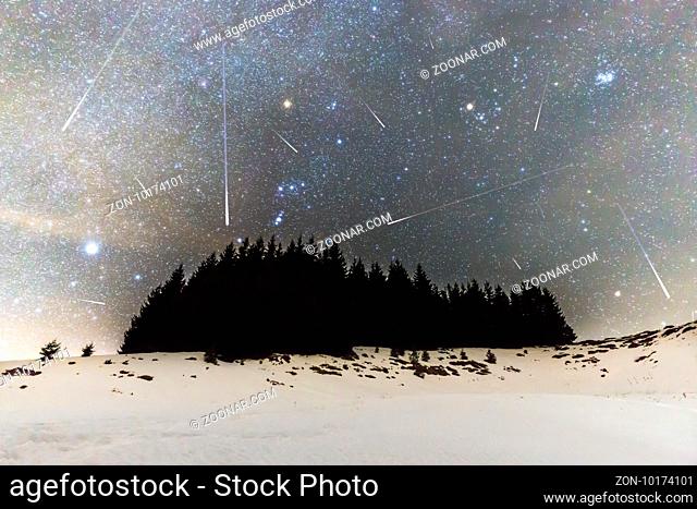 The Milky Way over the winter mountain landscape with pine trees in the foreground. Geminids Meteor Shower. Falling stars