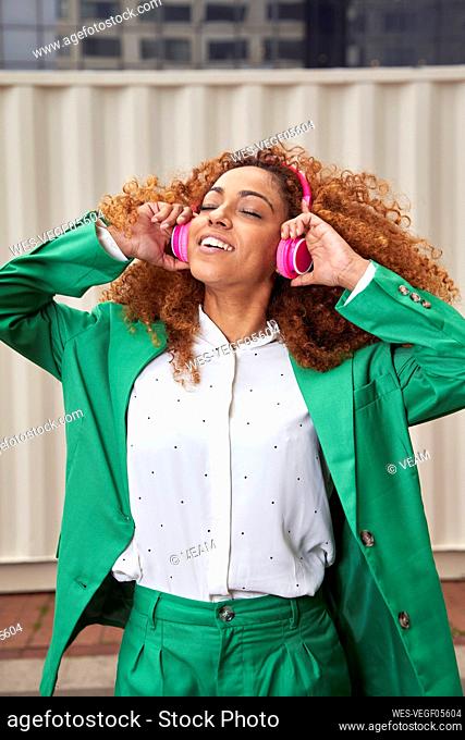 Smiling businesswoman with eyes closed listening music through wireless headphones