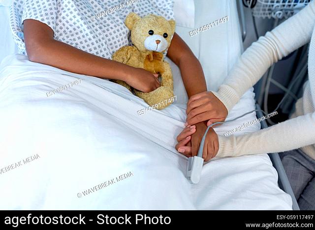Midsection of mixed race mother and sick daughter in hospital, girl holding teddy bear
