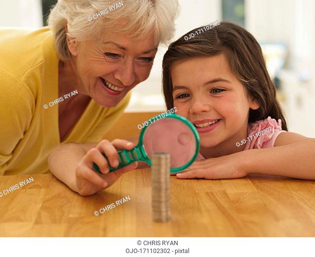 Grandmother and granddaughter looking at coins with magnifying glass